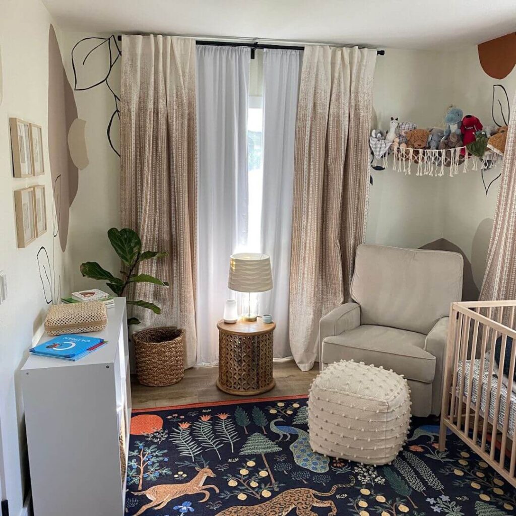 Cozy nursery room with beige patterned curtains, white armchair, colorful animal-themed rug, and wall-mounted stuffed animals shelf.