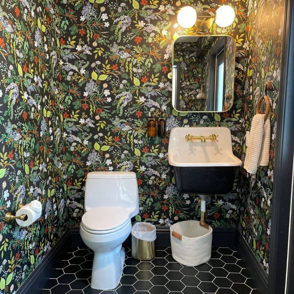 Stylish bathroom with floral wallpaper, hexagonal floor tiles, white porcelain sink with gold fixtures, and a mirrored wall light.