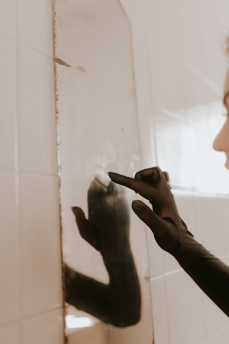 A gloved hand smudging a dirty mirror indoors.