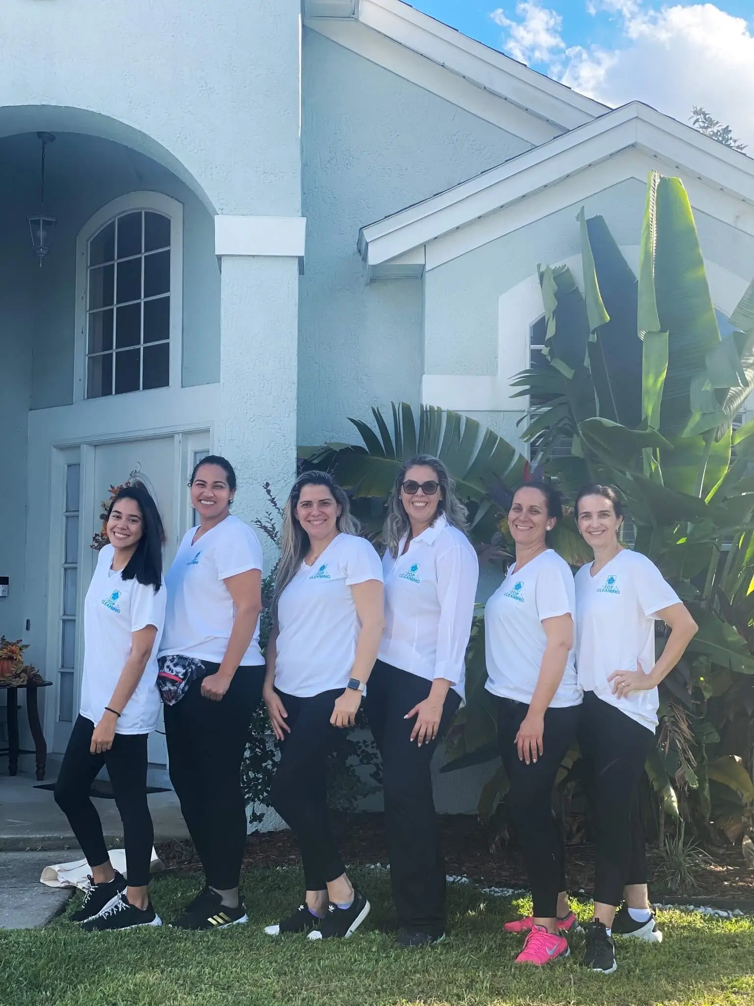 Learn About Us, Top Cleaning FL Team - all wearing white t-shirt and black pants in front of a light blue house and a green tree.