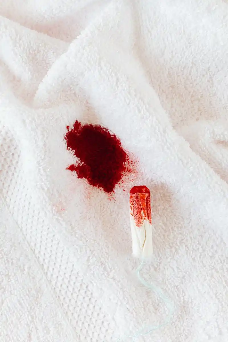 A close-up of a tampon and blood stain on a white towel, representing menstruation.